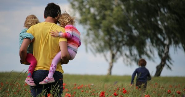 Photo by Juliane Liebermann man carrying to girls on field of red petaled flower