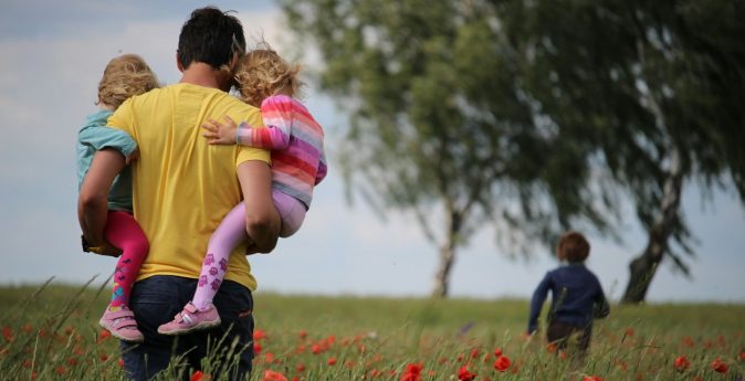 Photo by Juliane Liebermann man carrying to girls on field of red petaled flower